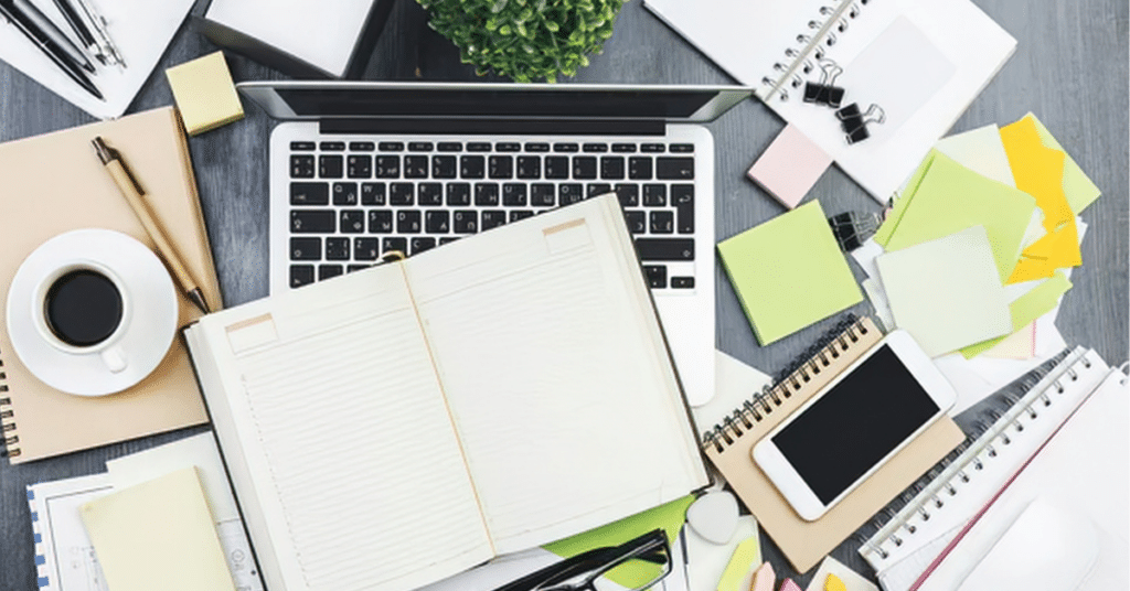 Cluttered desk with notebook, papers, and laptop