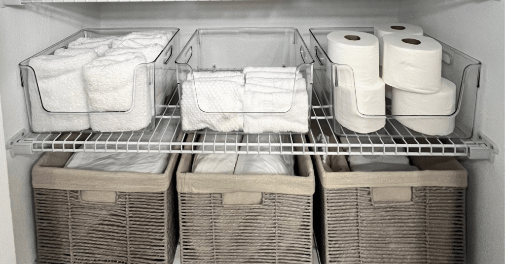 Linen closet with wire shelves organized with grey bins and acrylic bins