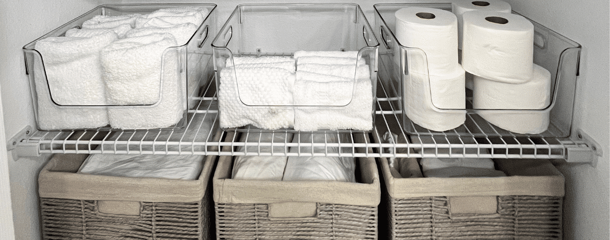 Linen closet with wire shelves organized with grey bins and acrylic bins