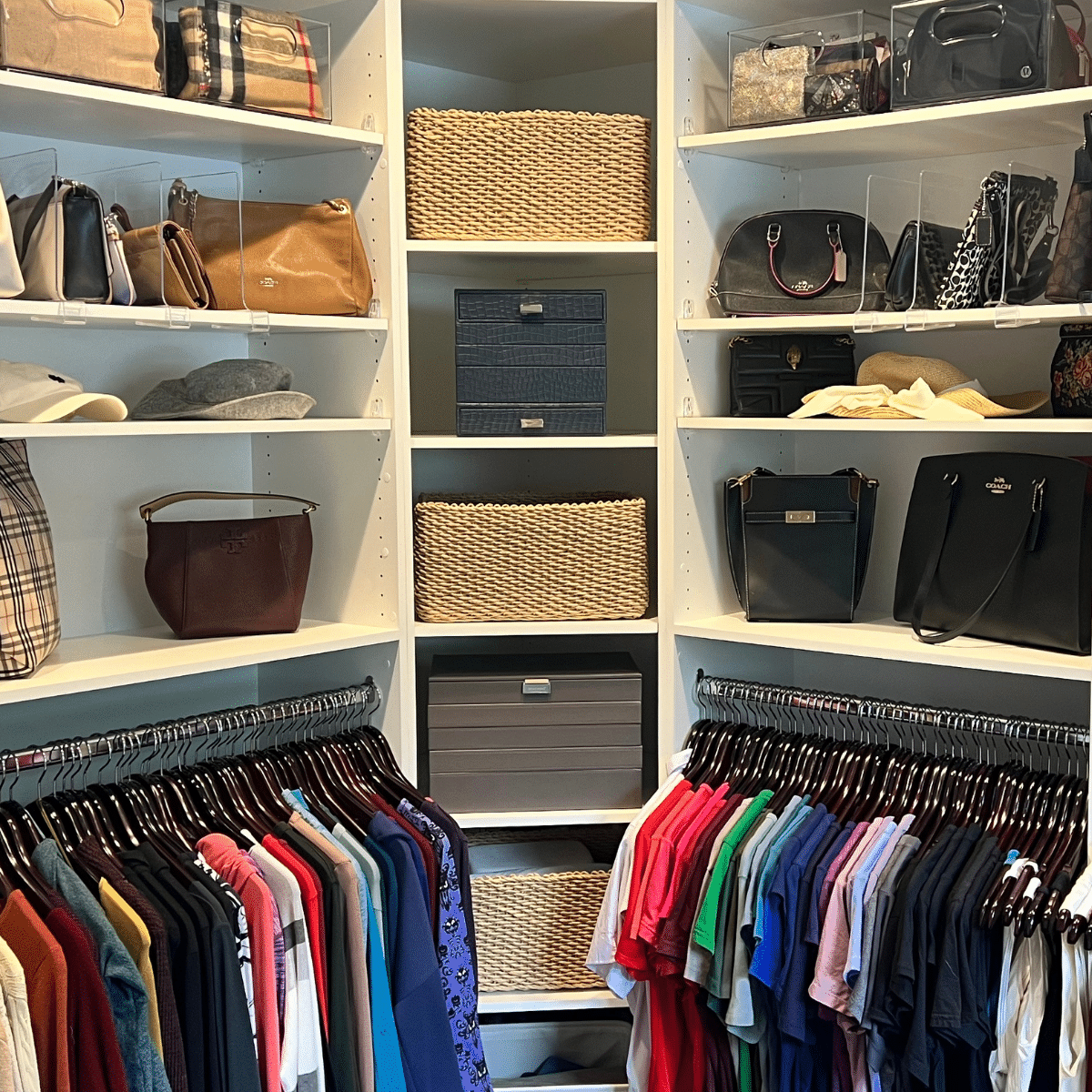 Organized walk in closer with purses and color coordinated clothing hanging on dark hangers